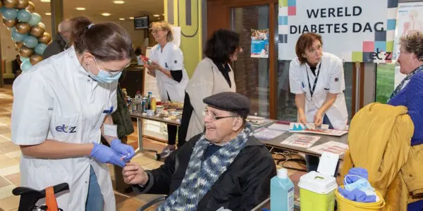 Op de voorgrond controleert diabetesverpleegkundige Marloes Valckx de bloedsuiker met een vingerprik bij een bezoeker.